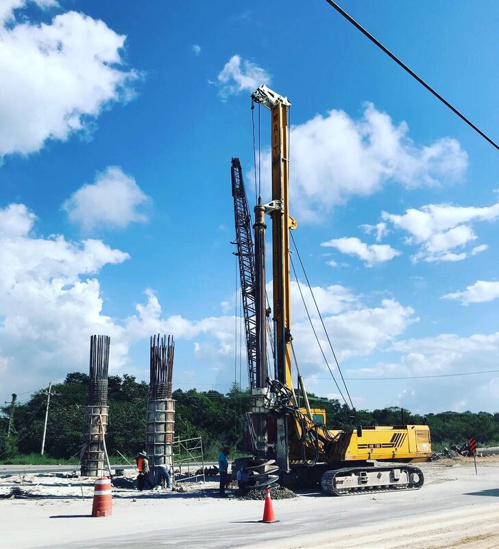 Grúa colocando pilote de concreto en cimentación de puente, junto a columnas terminadas